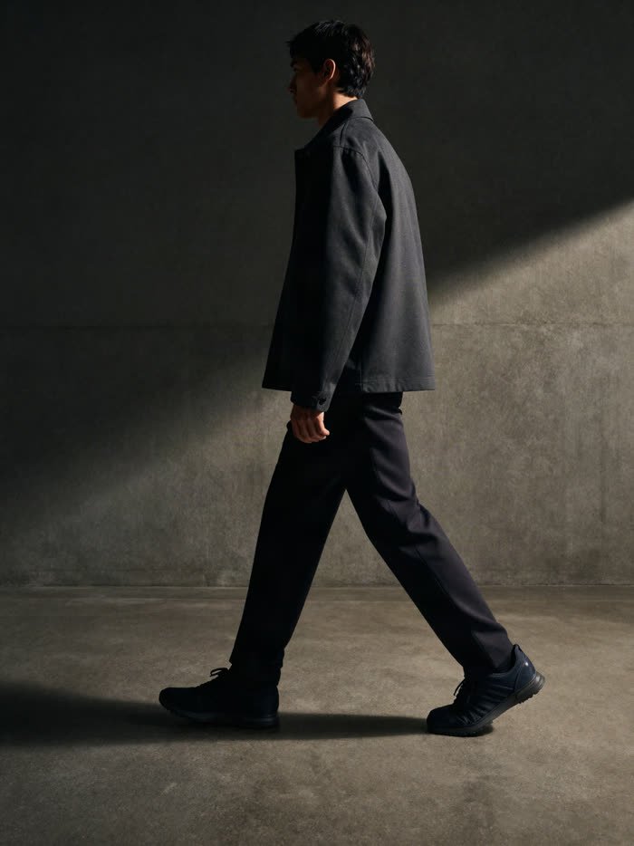A man mid stride in dark trousers and dark sneakers