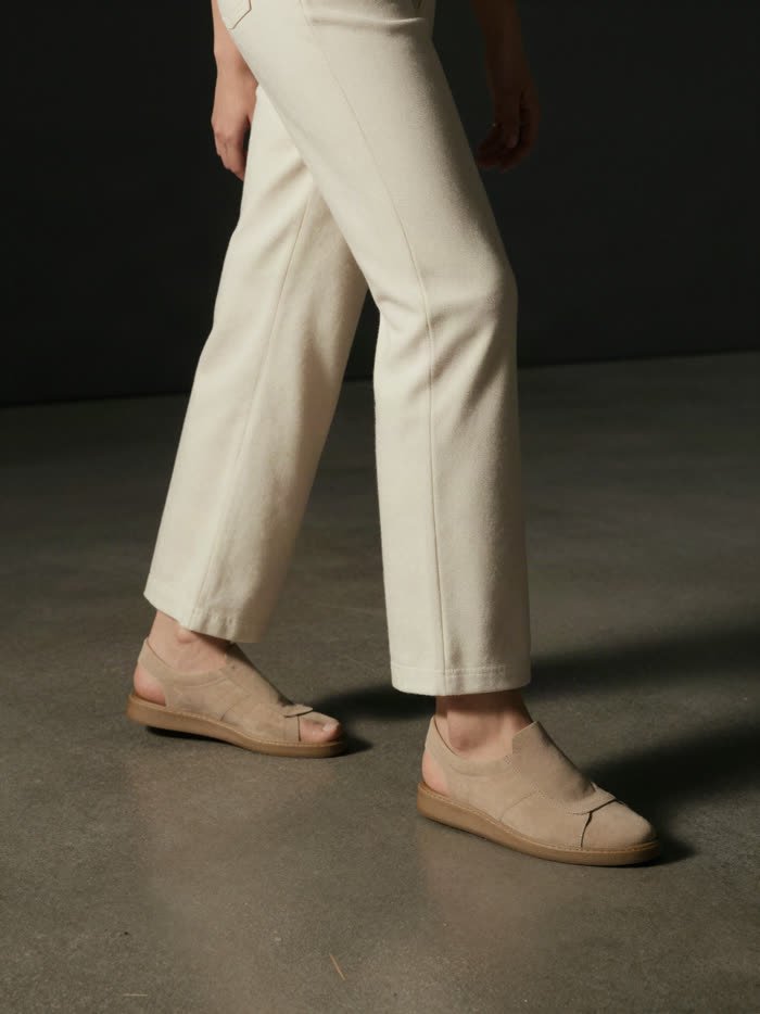 A woman mid step in cream trousers and sand sneakers