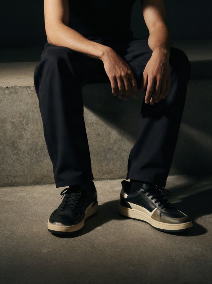 A man seated, dark trousers and black and cream sneakers